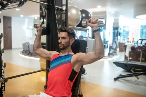 Young dark-haired man working on his arms on a gym machine and looking concentrated photo