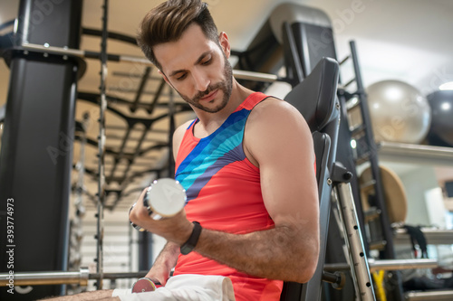 Young dark-haired man working on his arms with dumbbells photo