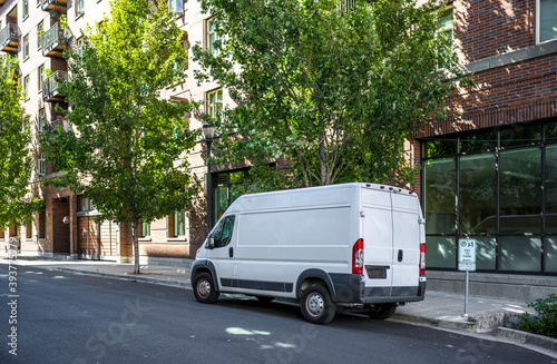 Compact industrial cargo mini van standing on the urban city street with multilevel apartments buildings