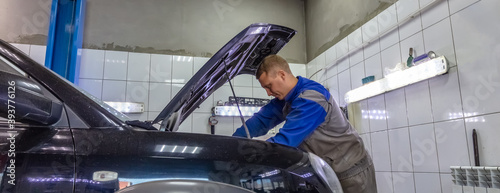 Auto mechanic under the hood, working on a car engine. Mechanic looks very serious and concentrated