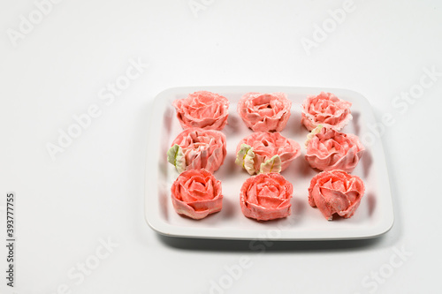 Pink marshmallows laid out in rows on a square white plate. white background.