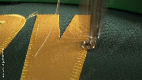 Machine embroiders golden letter on green fabric of uniform