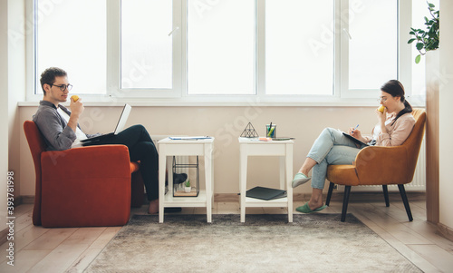 Caucasian man and his wife eating apple while lying in armchair and working on some business deals