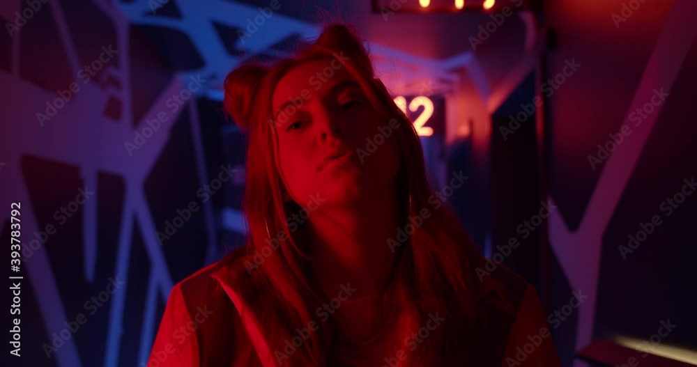 Close up view face and shoulders of young female person turning head and looking to camera. Attractive young woman posing while standing in neon lights. Concept of lifestyle Close up view face and shoulders of young female person turning head and looking to camera. Attractive young woman posing while standing in neon lights. Concept of lifestyle