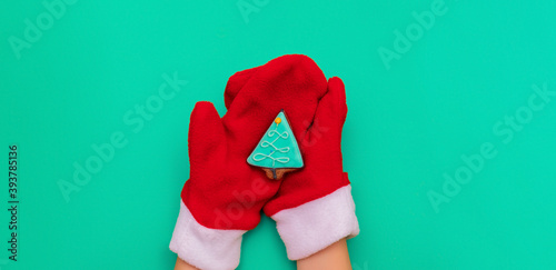 Gingerbread in the shape of a Christmas tree on the palms in red mittens of Santa Claus on a green background. Christmas, new year 2021. Flat lay, copy space, top view.