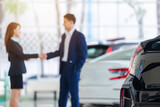 Selective focus on a new car and blur the dealership professional salesman and his client shaking hands. concept dealer Cars For Sale.