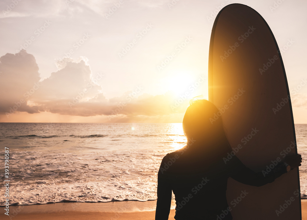 Silhouette of surfer woman carrying their surfboards on sunset beach with sun light.