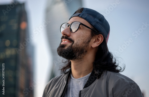 Attractive brunette man in cap wearing glasses in big city, head profile shot, street style © olezzo