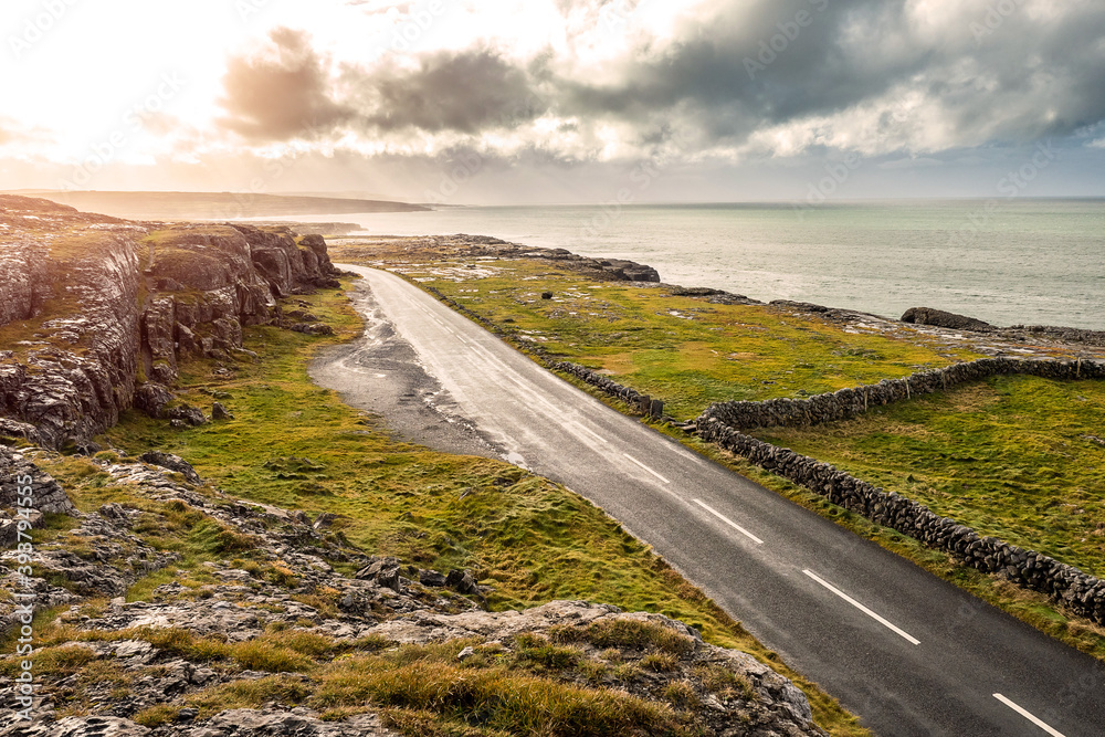 Small asphalt road on West coast of Ireland, part of Wild Atlantic Way route. Burren area, Ireland. Nobody. Cloudy sky. Green fields and famous rough terrain Small asphalt road on West coast of Ireland, part of Wild Atlantic Way route. Burren area, Ireland. Nobody. Cloudy sky. Green fields and famous rough terrain