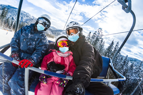 family wearing a medical mask during COVID-19 coronavirus on a snowy mountain at a ski resort