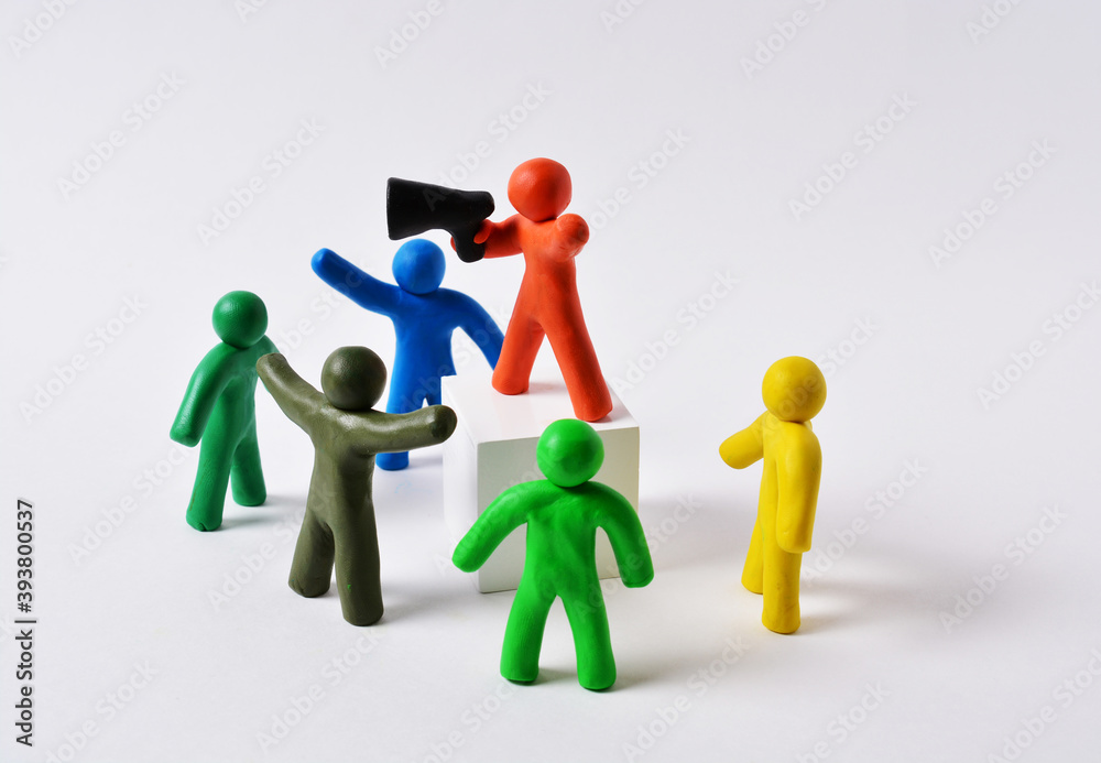Plasticine figures of people gathered in a group near a white cube with an orator, the orator speaks in megaphone, the concept of rallies, protests, announcements Plasticine figures of people gathered in a group near a white cube with an orator, the orator speaks in megaphone, the concept of rallies, protests, announcements