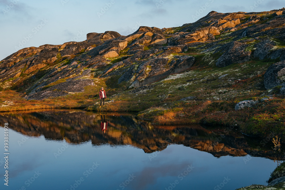 Small mountain lake on rocky sea coast, autumn colors, figure of young woman traveller enjoying the Beaty of nordic nature. 