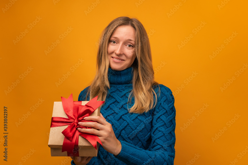 Charming young woman open a gift with red ribbon. Studio shot, yellow background. New Year, Birthday, Holiday concept Charming young woman open a gift with red ribbon. Studio shot, yellow background. New Year, Birthday, Holiday concept