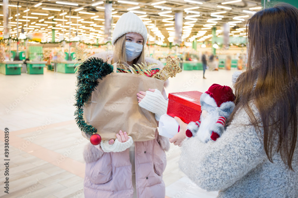 Young women in medical mask shopping for Christmas in mall. Xmas holidays in new Covid-19 reality. Selective focus