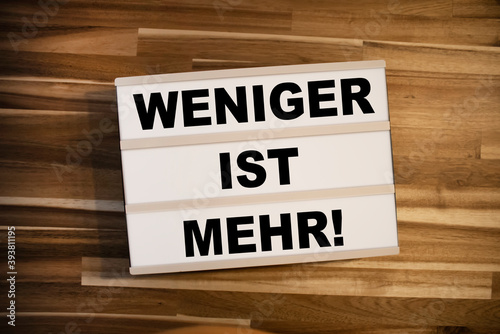 Lightbox or light box with the german words for Less is more - weniger ist mehr on wooden background table