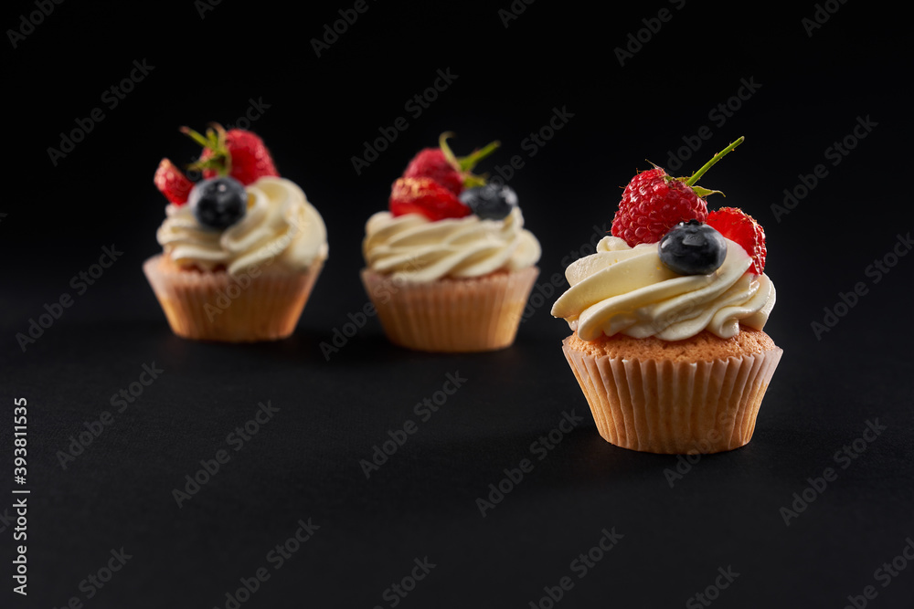 Tasty cupcakes with berries, isolated on black.