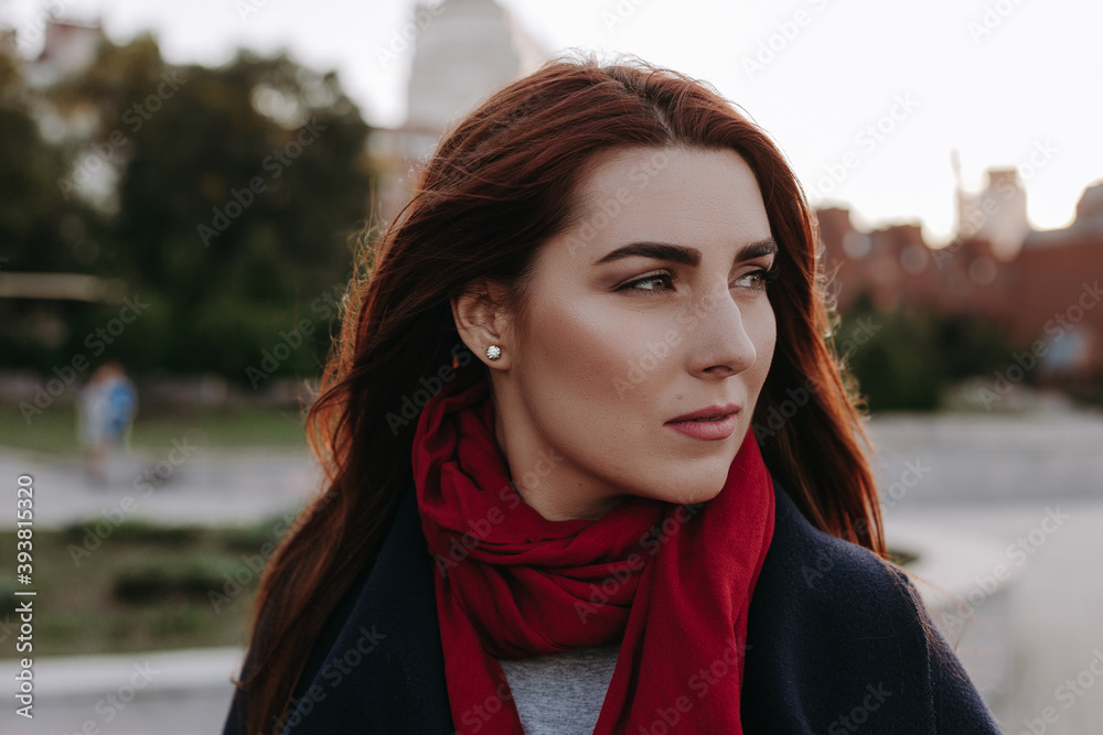 Pretty woman with green eyes and wide eyebrows and red hair posing on the city street  and smiling. Model dressed in warm clothes. Red scarf black coat and sunglasses. Romantic pretty female model