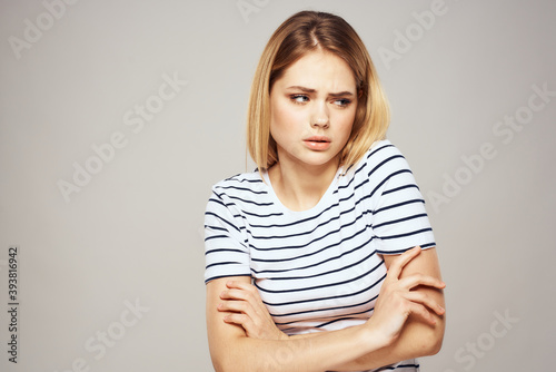 A woman in a striped T-shirt holds her hands in front of her emotions displeasure light background