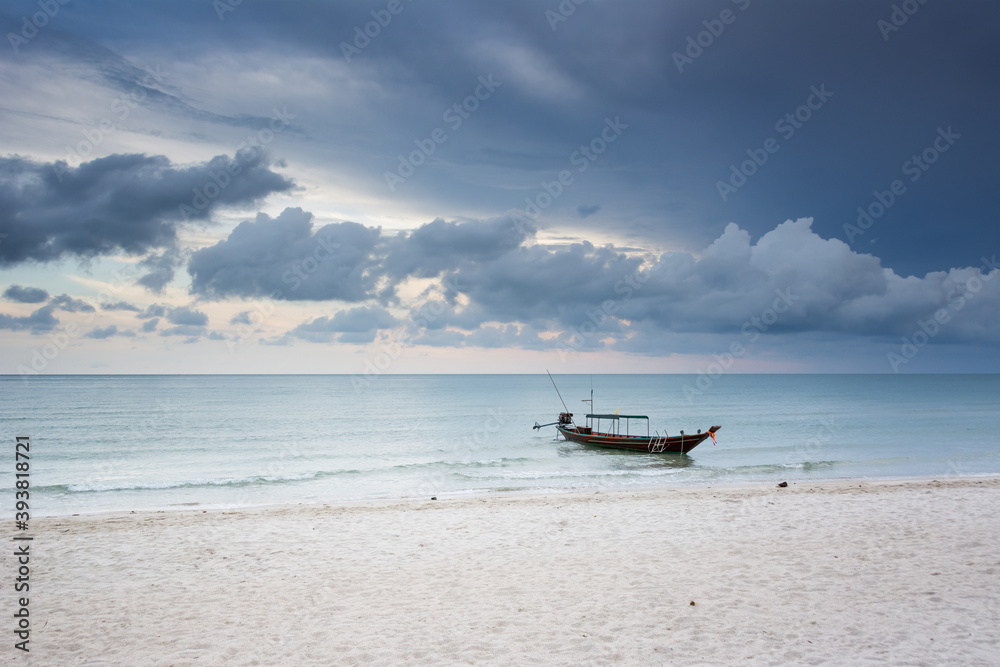 One long tail boat moored near the shore in Thailand. A dark sky like a storm is coming, low clouds on the horizon. Calm before the storm. White sand, nobody, just a boat. Bottle Beach, Koh Phangan