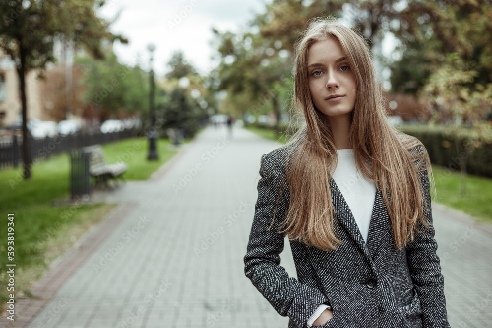 pretty woman in grey wool coat standing on the alley and looking in the camera pretty woman in grey wool coat standing on the alley and looking in the camera