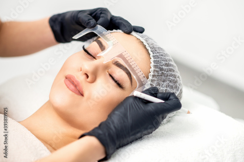 Beautician is measuring the brows with ruler before tattooing eyebrows photo