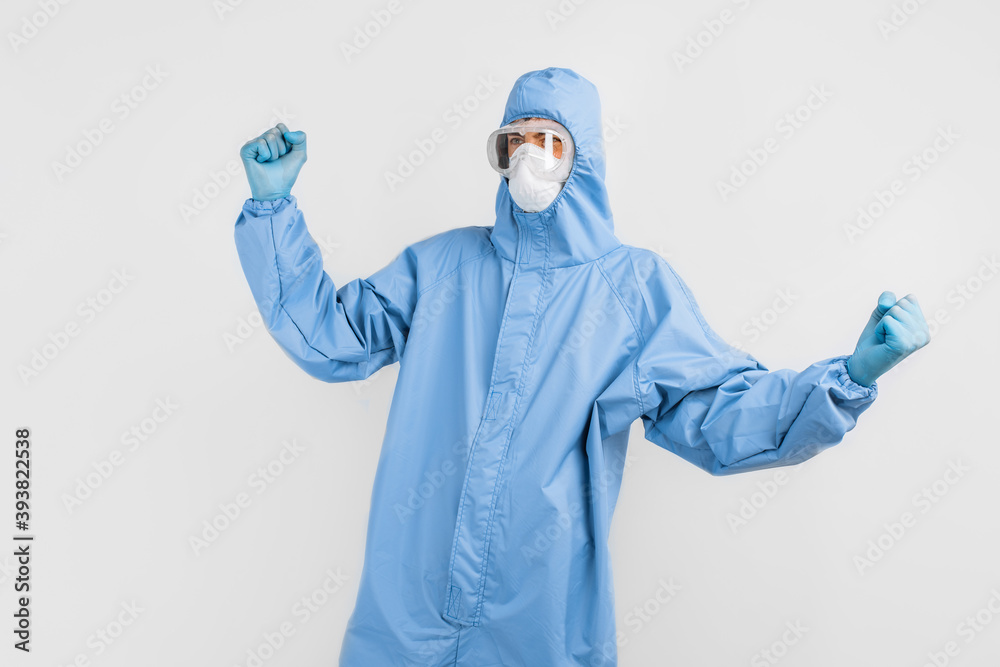 Man doctor in a protective suit to fight Covid-19, wearing glasses, a mask and gloves, shows a victory gesture on a white background Man doctor in a protective suit to fight Covid-19, wearing glasses, a mask and gloves, shows a victory gesture on a white background