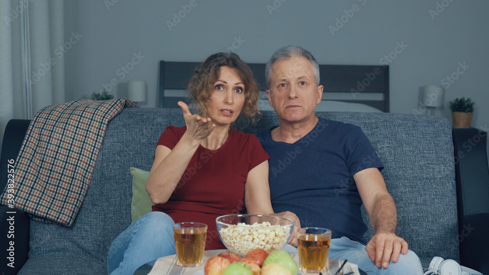 A man and a woman watching horror movies on TV and eating popcorn.