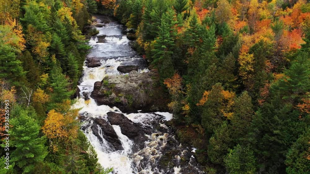 Beautiful autumn aerial flying over Upper Potato Falls with heavy water flow cascading over large rock formations and with yellow orange and green deciduous and evergreen trees lining the river banks. Beautiful autumn aerial flying over Upper Potato Falls with heavy water flow cascading over large rock formations and with yellow orange and green deciduous and evergreen trees lining the river banks.