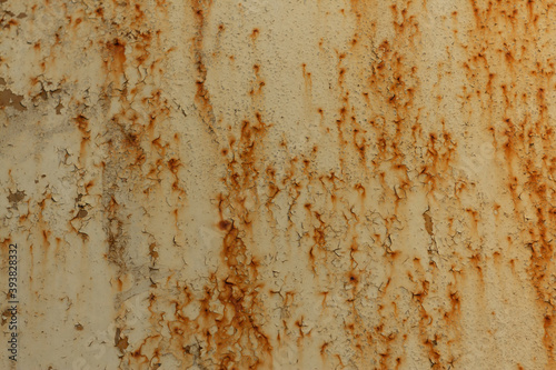 Texture of a light yellow metal plate with peeling paint, splashes and streaks of rust close up