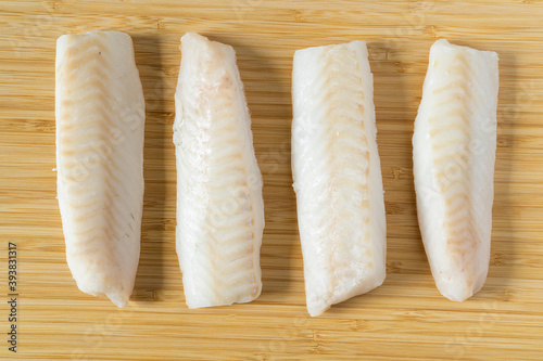 Fresh iced pieces of cod fish loins or fillets on wooden cutting board. Top view.