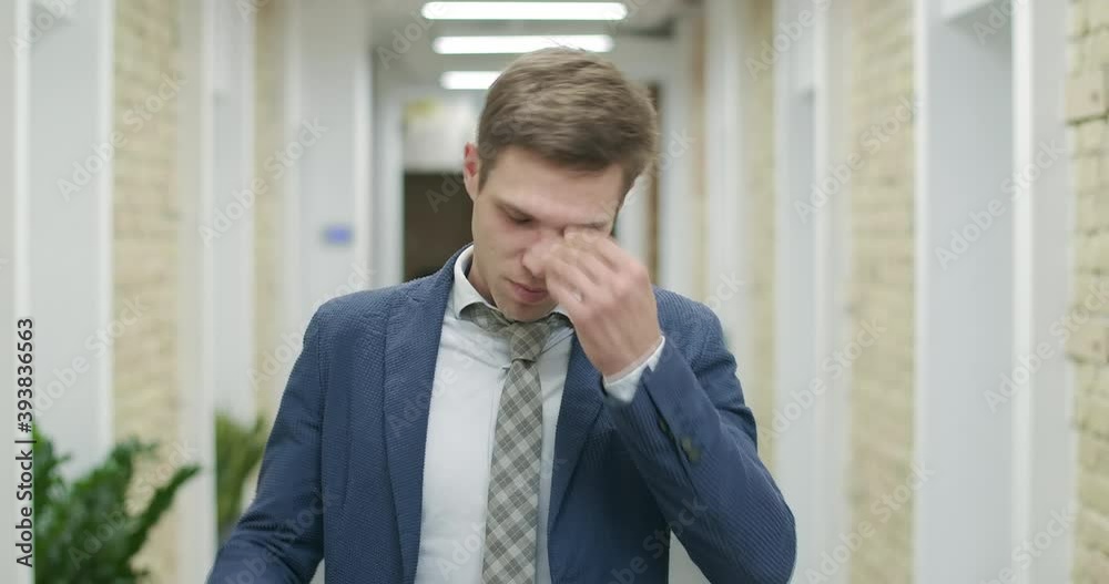Tired young businessman taking off eyeglasses. rubbing eyes, and looking at camera. portrait of stressed confident Caucasian man posing in office corridor. Cinema 4k ProRes HQ.