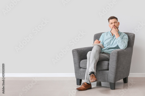 Male psychologist sitting in armchair near light wall