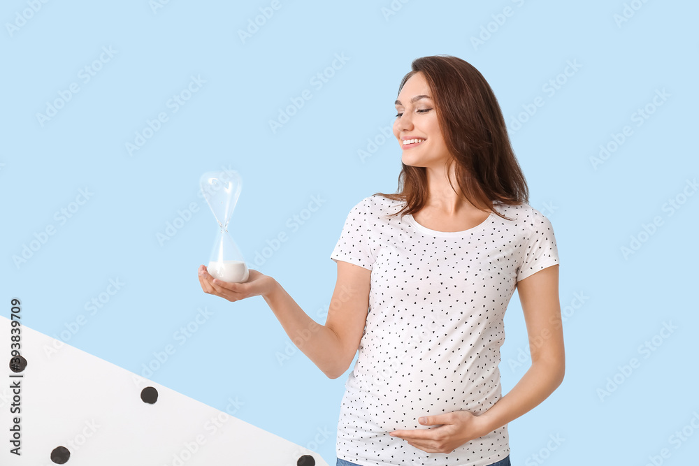 Young pregnant woman with hourglass on color background Young pregnant woman with hourglass on color background
