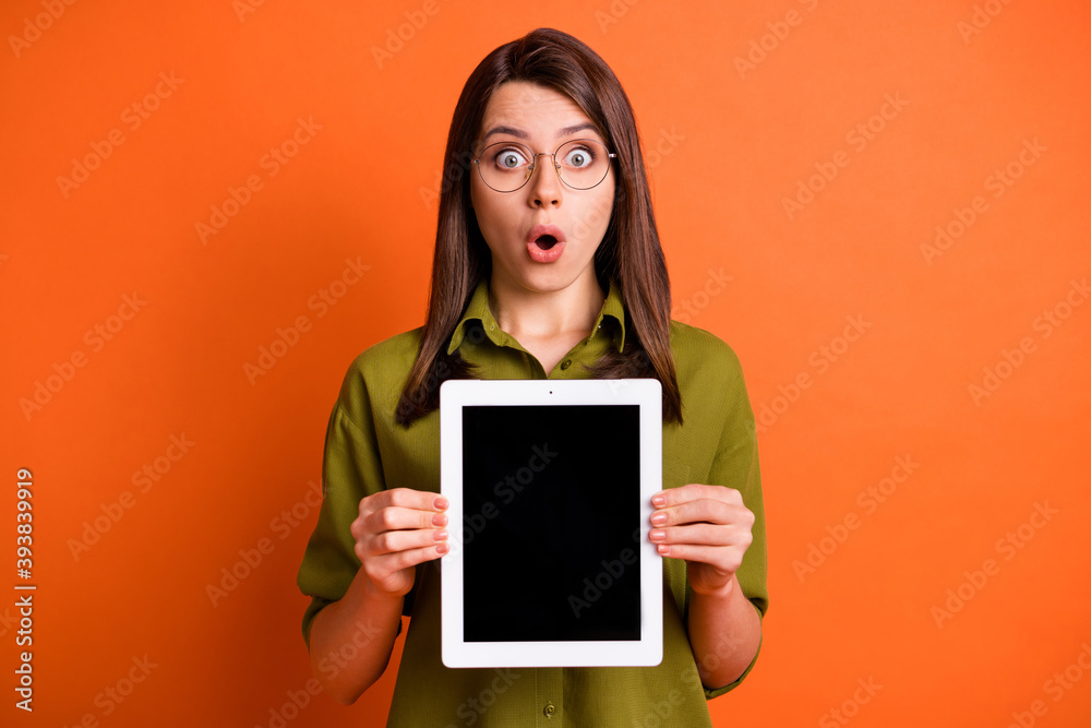 Photo portrait of amazed female student keeping tablet showing touchscreen copyspace isolated on vibrant orange color background Photo portrait of amazed female student keeping tablet showing touchscreen copyspace isolated on vibrant orange color background
