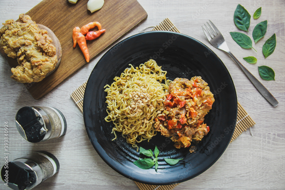 Flat lay, top view. Fried instant noodles with chicken spicy on the black plate and fried chicken on wooden board on wooden table Flat lay, top view. Fried instant noodles with chicken spicy on the black plate and fried chicken on wooden board on wooden table