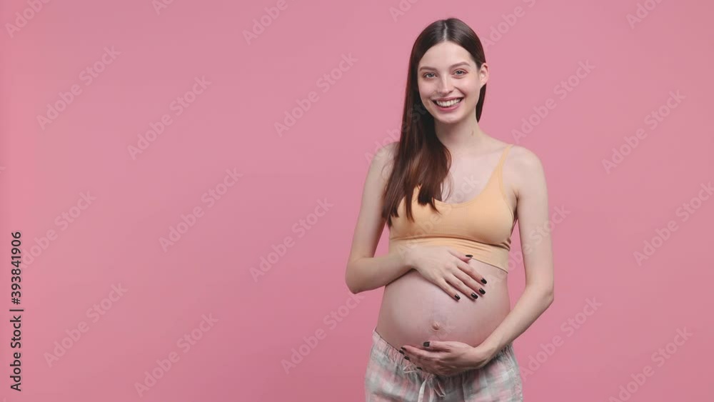 Smiling pregnant woman future mom in basic top stroking keep hands on belly tummy with baby waving meet greet hi isolated on pastel pink background studio Maternity family pregnancy gynecology concept Smiling pregnant woman future mom in basic top stroking keep hands on belly tummy with baby waving meet greet hi isolated on pastel pink background studio Maternity family pregnancy gynecology concept