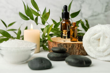 Foto auf Acrylglas Massagesalon Schönheitsbehandlungsartikel für Spa-Behandlungen auf weißem Holztisch mit grüner Pflanze. Massagesteine, ätherische Öle und Meersalz mit brennender Kerze  © ronstik