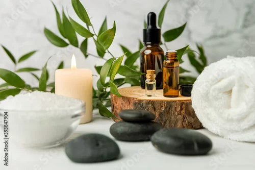 Obraz beauty treatment items for spa procedures on white wooden table with green plant. massage stones, essential oils and sea salt with burning candle