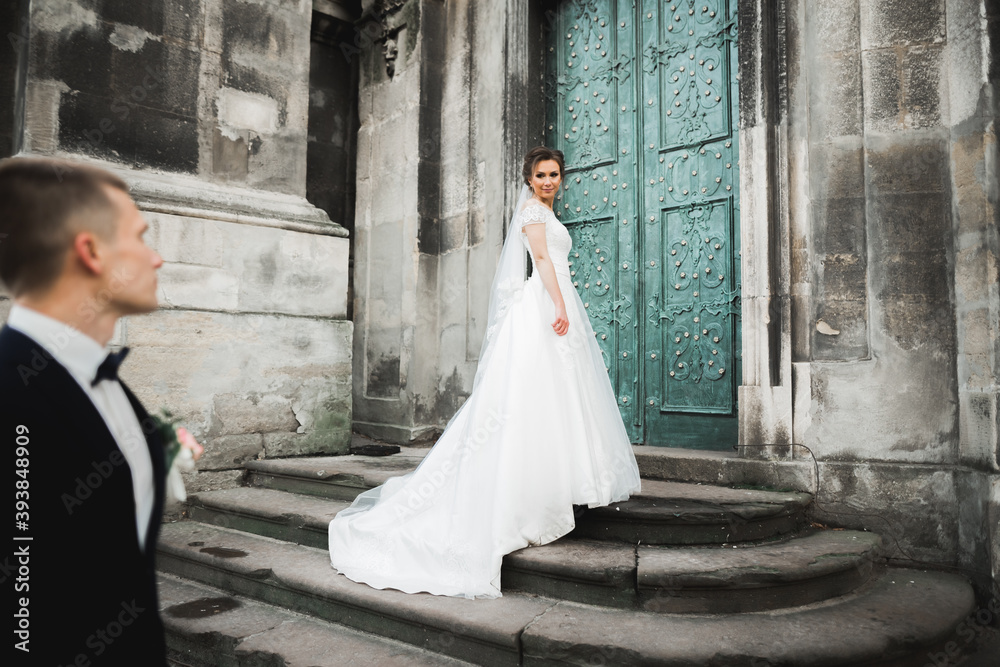 Lovely happy wedding couple, bride with long white dress posing in beautiful city Lovely happy wedding couple, bride with long white dress posing in beautiful city