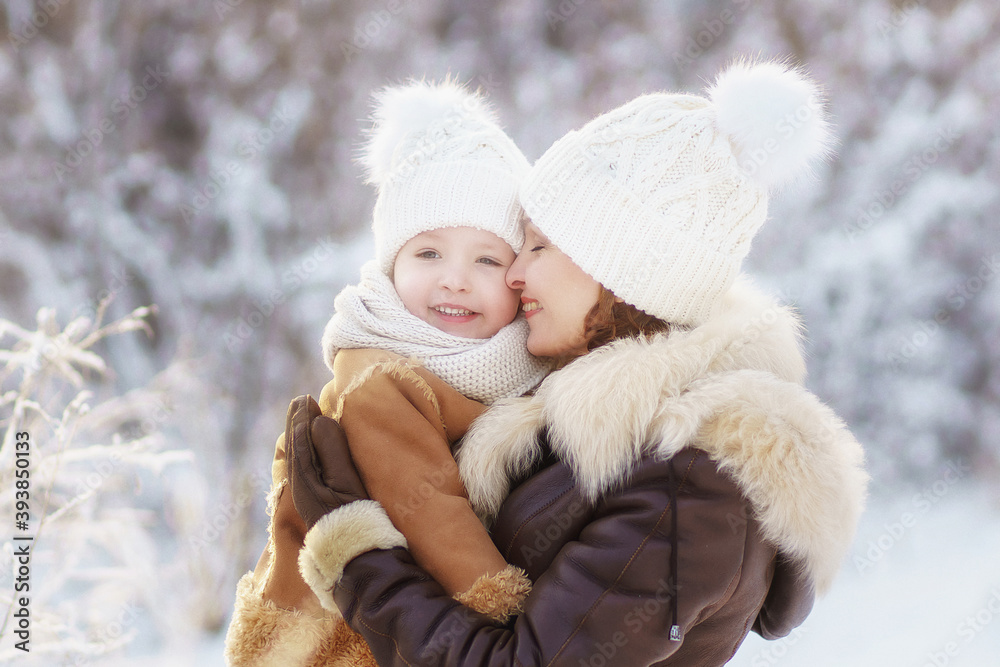 Fototapeta premium mother and daughter in brown fur coats hug during a walk through the winter forest. lots of snow around. bright emotion.