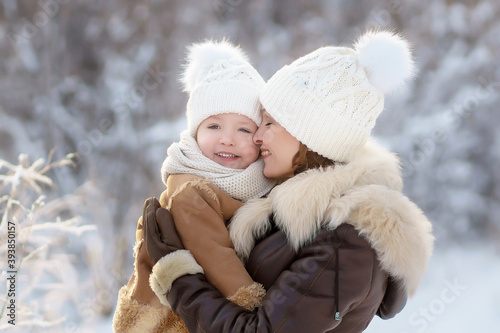 mother and daughter in brown fur coats hug during a walk through the winter forest. lots of snow around. bright emotion.