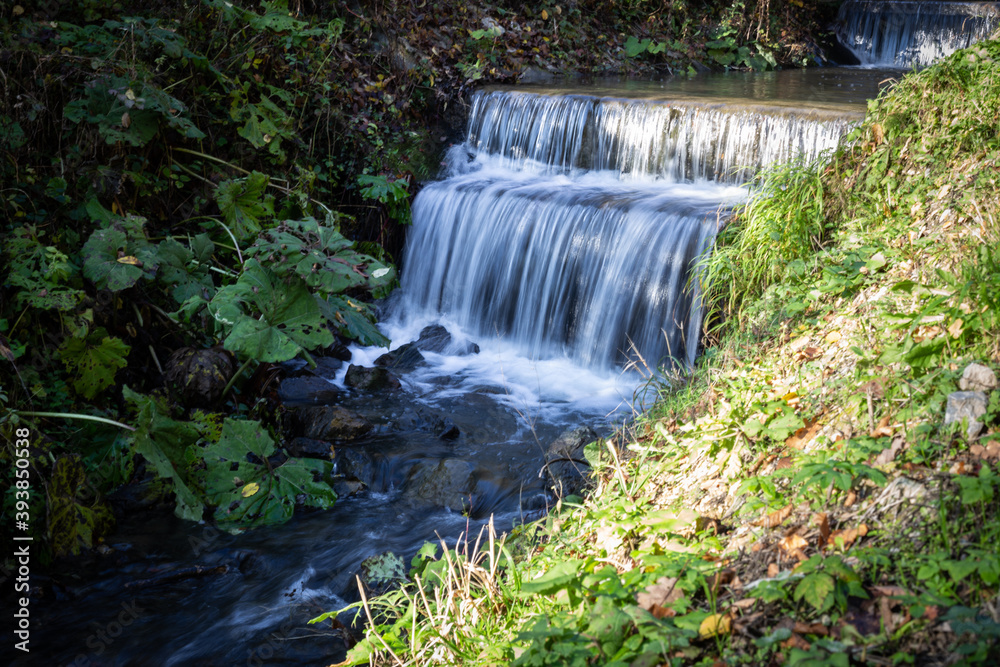 Obraz premium A mountain brook in late autumn. Small stream with waterfall captured in motion blur.