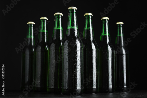 Glass bottles of beer on table against black background