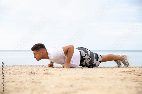 Muscular man doing push up on beach. Body training