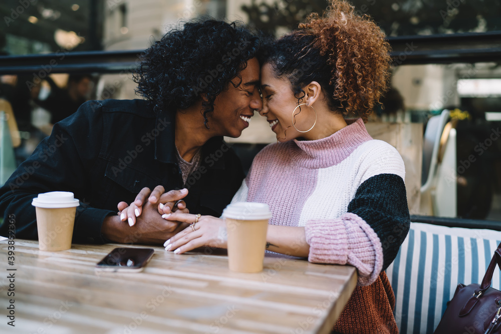 Cheerful multiethnic loving couple touching noses sitting in cafe Cheerful multiethnic loving couple touching noses sitting in cafe