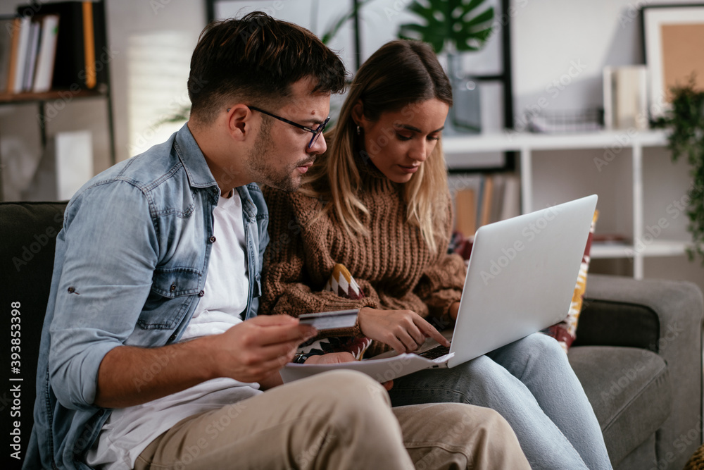 Young couple using credit card and laptop at home. Boyfriend and girlfriend buying online.. Young couple using credit card and laptop at home. Boyfriend and girlfriend buying online..