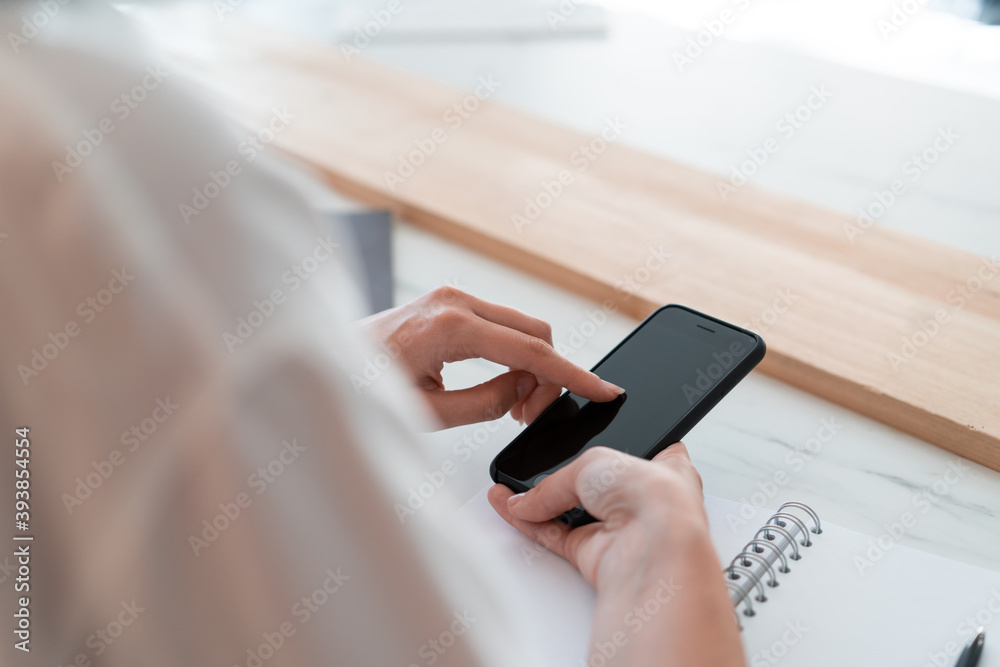 Top view of woman office manager hands with black smartphone, typing a message, finger on the screen. Blurred background of office table desk. Concept of message