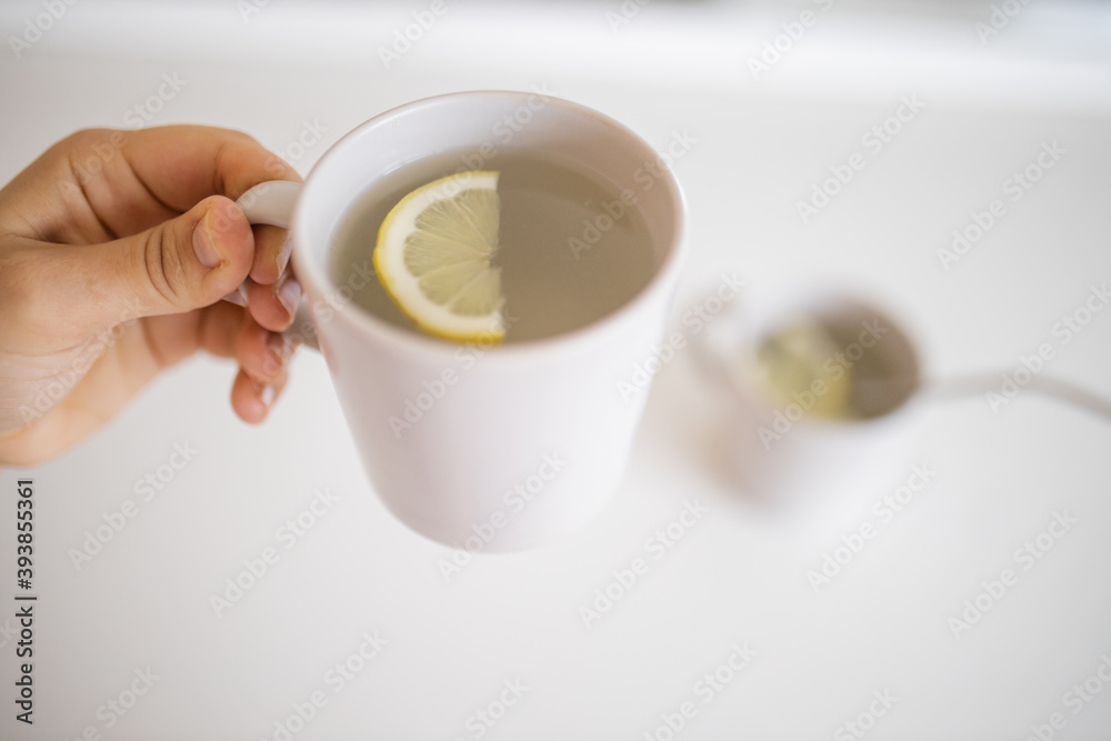 Hand holding a cup of lemon tea with a lemon slice inside Hand holding a cup of lemon tea with a lemon slice inside