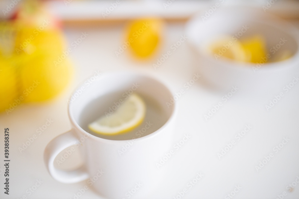 Cup of lemon tea on a white table surrounded by lemons