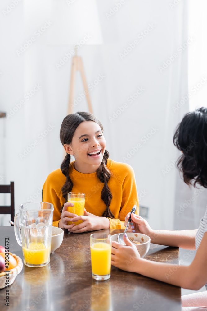 Hispanic girl smiling at mother during breakfast with orange juice Hispanic girl smiling at mother during breakfast with orange juice